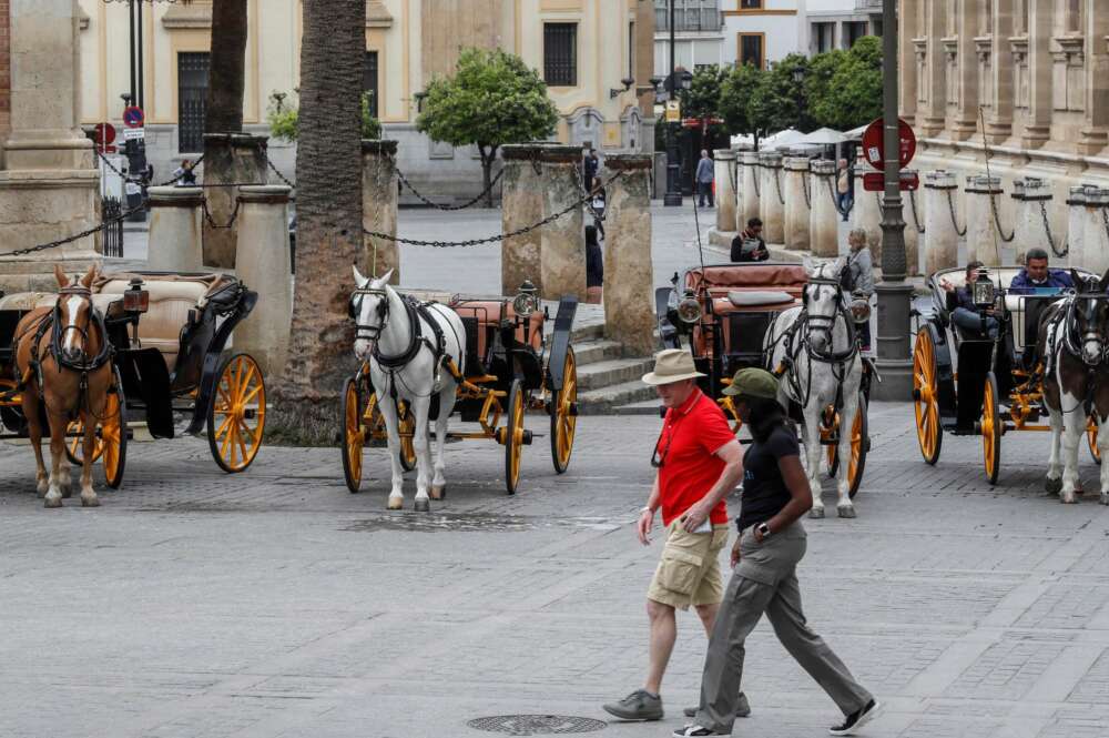 GRAF6736. SEVILLA (ESPAÑA), 14/03/2020.- Una pareja de turistas pasa junto a coches de caballos este sábado en Sevilla. El presidente de la Junta, Juanma Moreno, ha sostenido que la suspensión de la Semana Santa en Sevilla, acordada este mismo sábado, "es una medida responsable y necesaria para frenar el avance del coronavirus". EFE/José Manuel Vidal