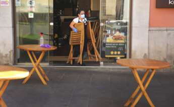 Una trabajadora de un establecimiento de hostelería saca las sillas a la terraza.