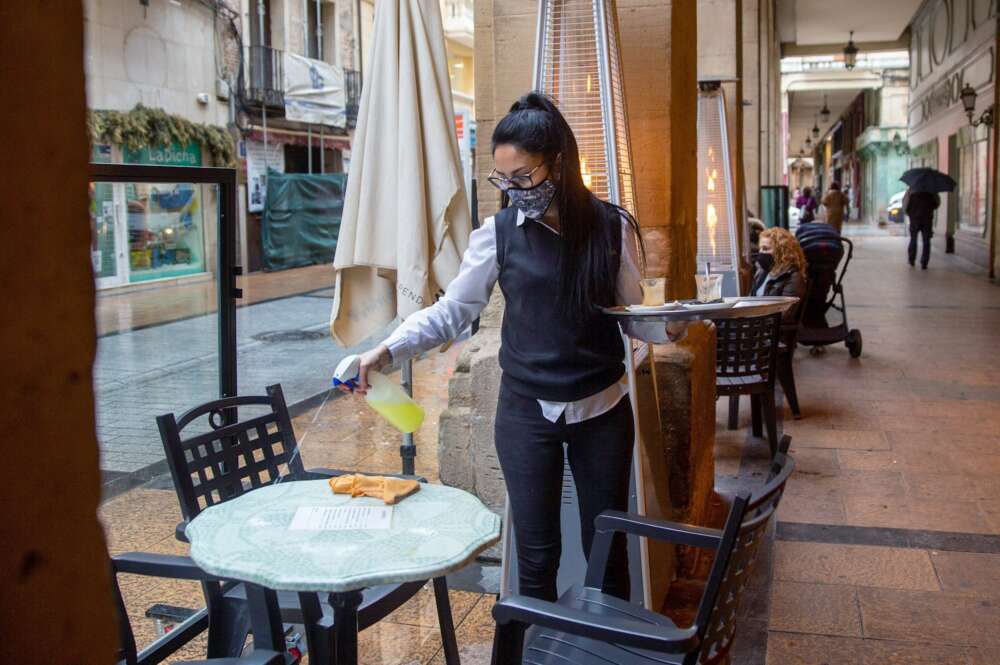 Una camarera desinfecta una mesa