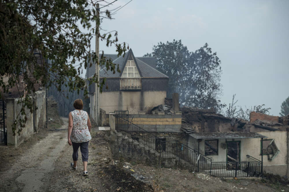 Una vecina de la localidad de Alixo (O Barco de Valdeorras) pasa ante las casa calcinadas por las llamas. Galicia que vuelve a afrontar una jornada decisiva para extinguir los incendios forestales que afectan a las provincias de Ourense y Lugo y que mantienen en riesgo varios núcleos de población. EFE/ Brais Lorenzo