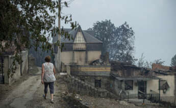 Una vecina de la localidad de Alixo (O Barco de Valdeorras) pasa ante las casa calcinadas por las llamas. Galicia que vuelve a afrontar una jornada decisiva para extinguir los incendios forestales que afectan a las provincias de Ourense y Lugo y que mantienen en riesgo varios núcleos de población. EFE/ Brais Lorenzo