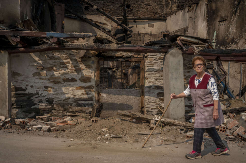 Una vecina pasea junto a una vivienda calcinada tras el incendio forestal acontecido en el pueblo de Alixo (O Barco de Valdeorras), en Ourense / Brais Lorenzo (EFE)