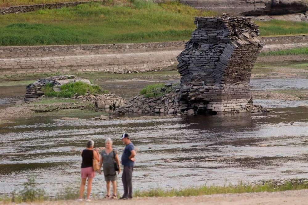 Tres personas junto al río Miño, cuyo bajo caudal ha dejado a la vista las ruinas del antiguo Portomarín, que en los años 60 del siglo pasado fue anegado por el embalse de Belesar