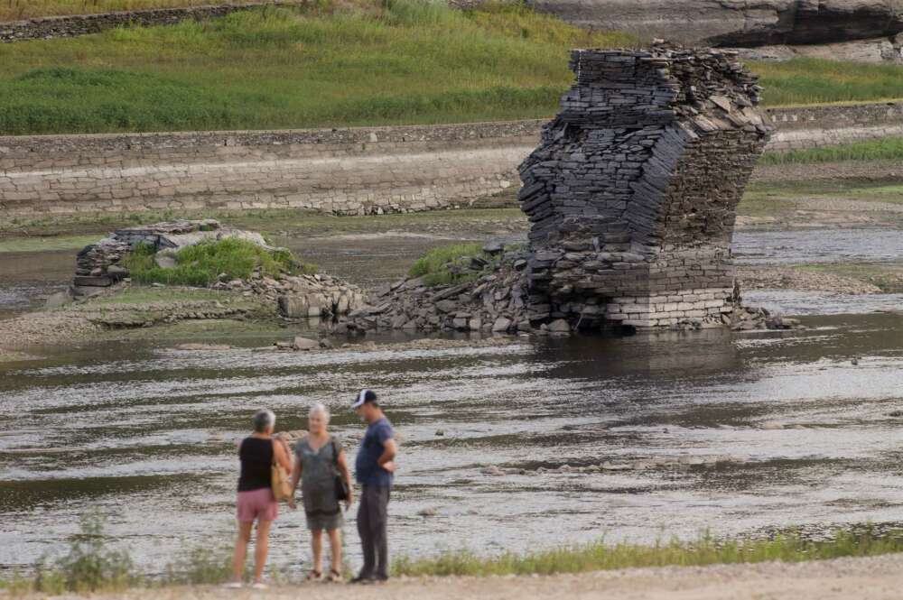 Tres personas junto al río Miño, cuyo bajo caudal ha dejado a la vista las ruinas del antiguo Portomarín, que en los años 60 del siglo pasado fue anegado por el embalse de Belesar / Europa Press