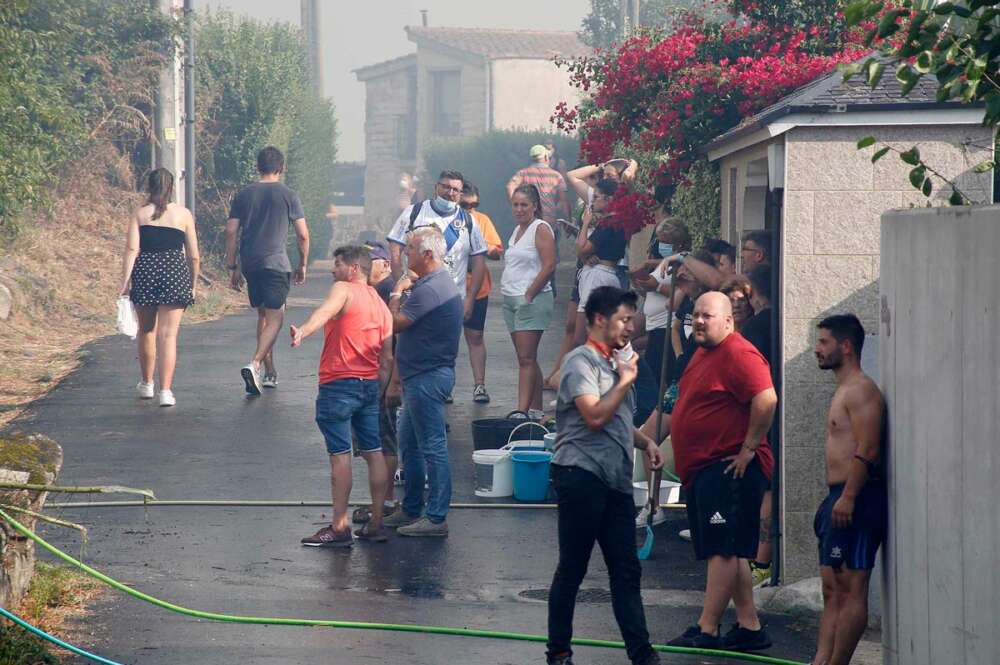 Los vecinos de la parroquia de Meira con cubos de agua y mangueras para sofocar el fuego, a 22 de agosto, en la parroquia de Meira, en Moaña, Pontevedra, Galicia (España)