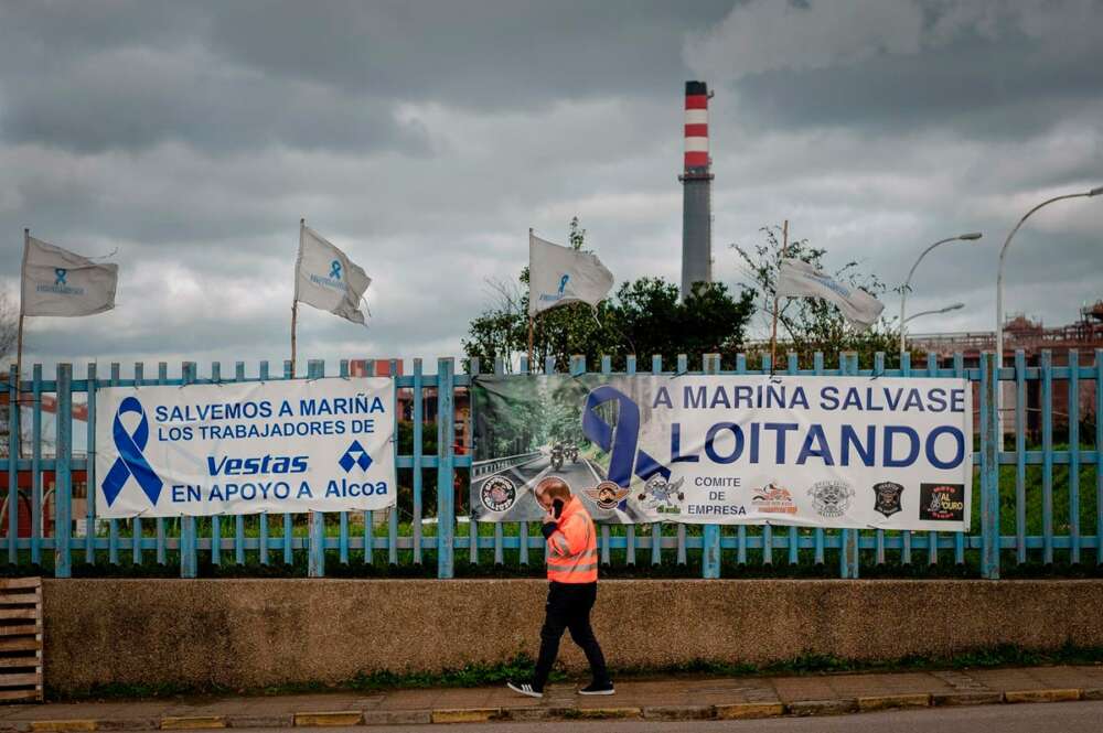 Una persona pasa delante de una pancarta, colocada por los trabajadores en la valla de la fábrica de Alcoa en San Cibrao