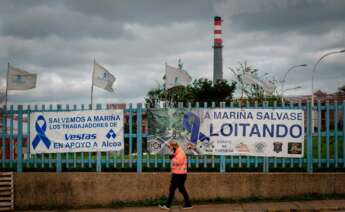 Una persona pasa delante de una pancarta, colocada por los trabajadores en la valla de la fábrica de Alcoa en San Cibrao