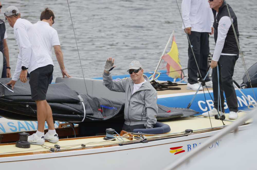 El rey emérito Juan Carlos I saluda desde la embarcación a su llegada este jueves al Real Club Náutico de Sanxenxo, tras haber viajado hasta la localidad para preparar la regata en la que pretende participar este fin de semana en la localidad gallega. EFE/Lavandeira Jr