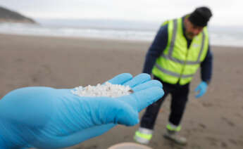 Un operario de TRAGSA coge con la mano pellets de plástico, en la playa Otur, a 9 de enero de 2024, en Valdés, Asturias (España)