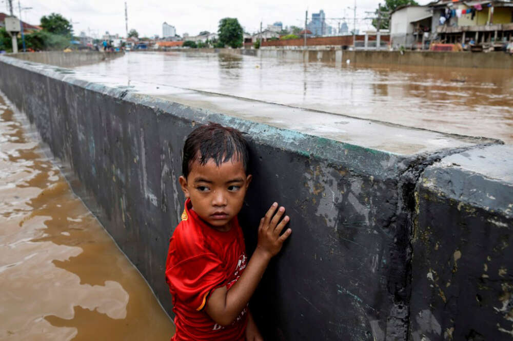 Un niño se protege tras un muro en una carretera inundada de Yakarta (Indonesia) en 2020