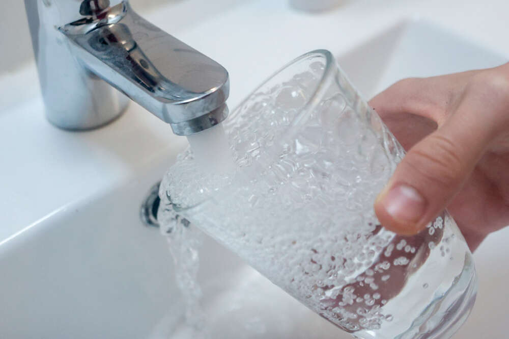 Una persona llena un vaso de agua de un grifo