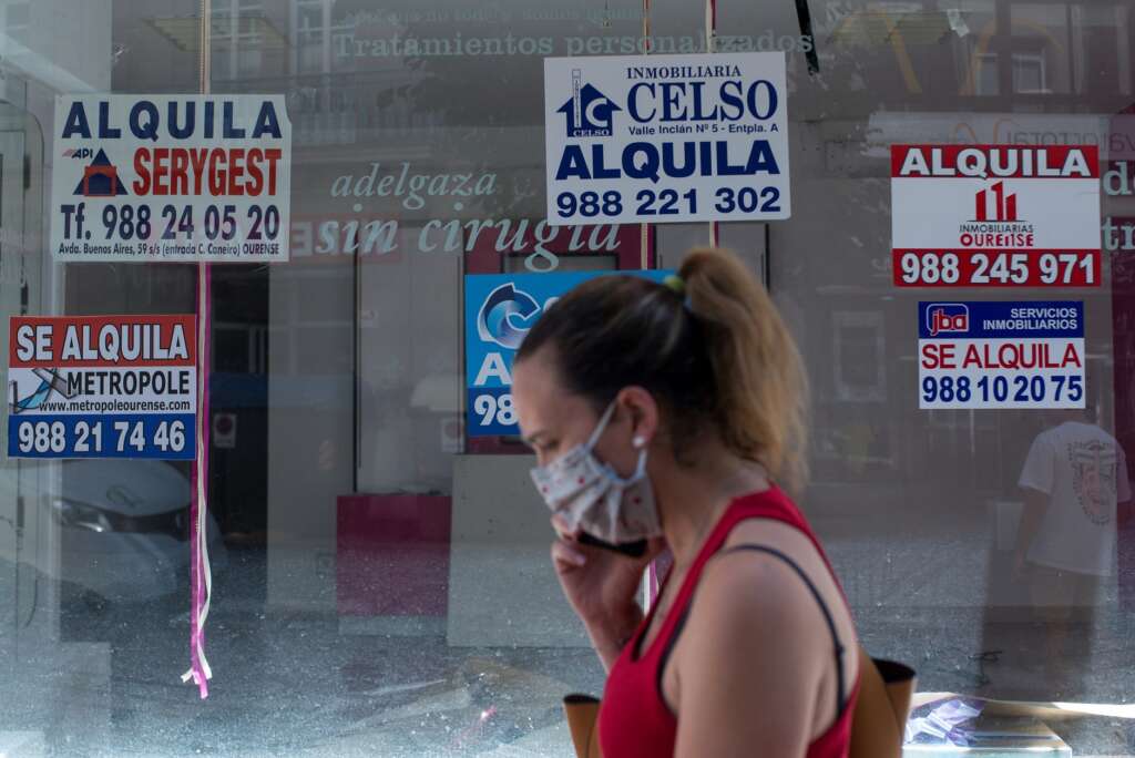 Una mujer con mascarilla pasa ante un comercio cerrado con varios carteles que anuncian su alquiler, el 10 de julio de 2020, en Orense | EFE/BL/Archivo