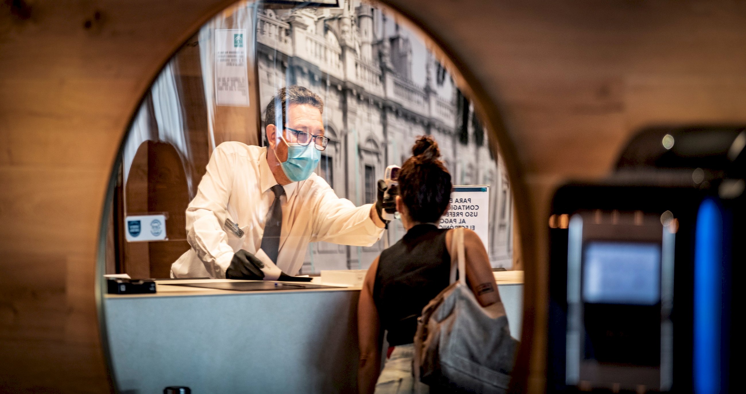 Recepción del Hotel Zenit de Sevilla donde se atiende a una clienta con las medidas de seguridad, mascarillas, gel desinfectante... por la pandemia de coronavirus. Foto: Efe/ José Manuel Vidal