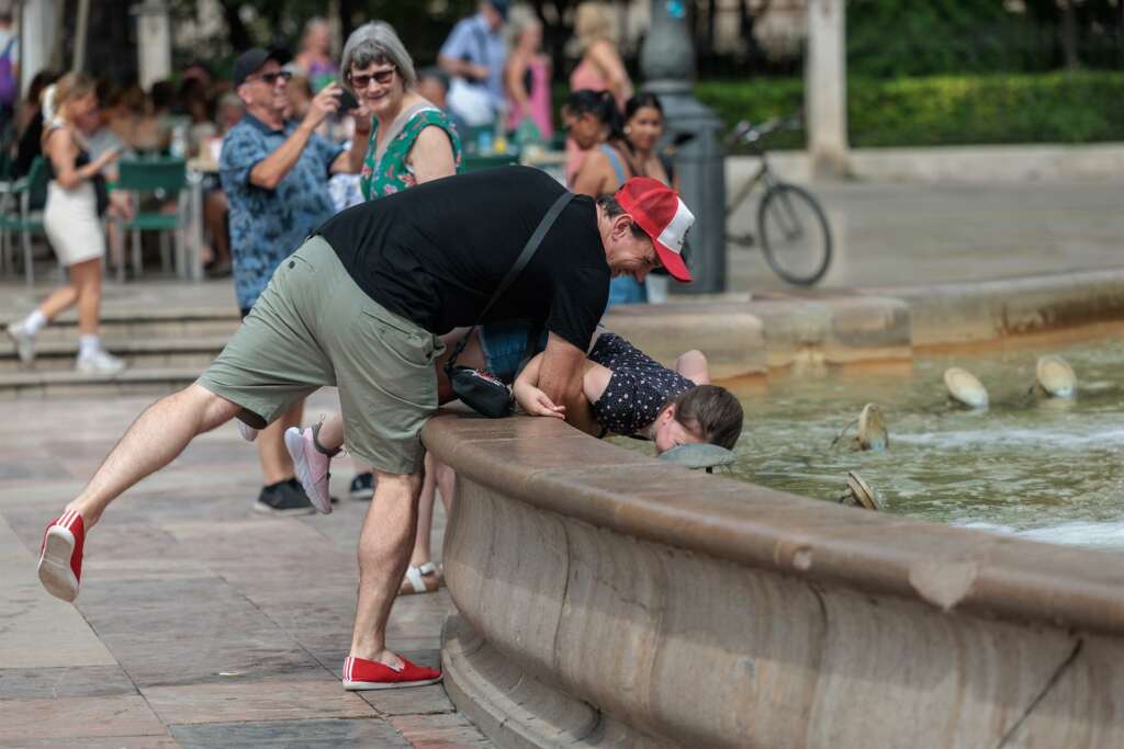 Un hombre refresca a su hijo en una fuente. EFE/Biel Aliño