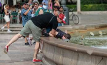 Un hombre refresca a su hijo en una fuente. EFE/Biel Aliño