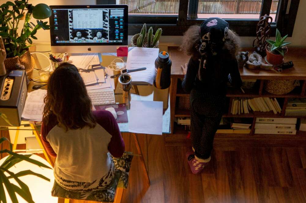 Una mujer realiza teletrabajo en su casa mientras su hija juega a su lado, el 16 de marzo de 2020, primer día laboral de aplicación del estado de alarma | EFE/Archivo