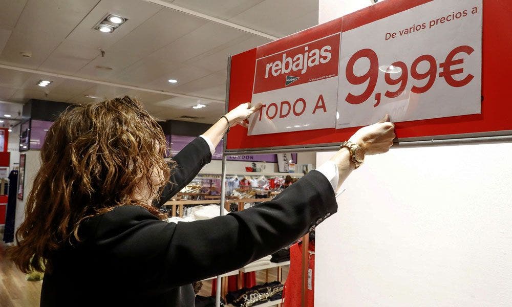 Una persona coloca un cartel de rebajas en El Corte Inglés