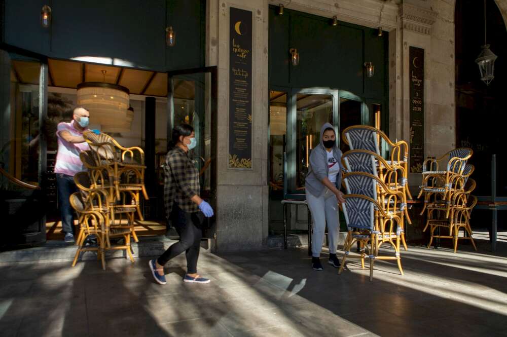 Dos trabajadores recogen la terraza de un bar del centro de Barcelona, afectado por las restricciones sanitarias del coronavirus /EFE/Enric Fontcuberta