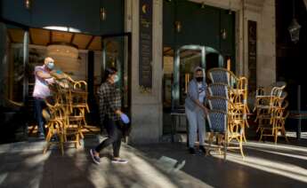 Dos trabajadores recogen la terraza de un bar del centro de Barcelona, afectado por las restricciones sanitarias del coronavirus /EFE/Enric Fontcuberta