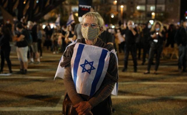 Uno de los manifestantes ataviado con mascarillas y la bandera de Israel. | EFE
