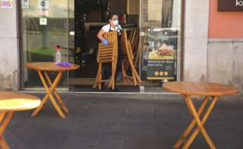 Una trabajadora de un establecimiento de hostelería saca las sillas a la terraza, vacía de clientes por la pandemia de coronavirus. EFE/Archivo