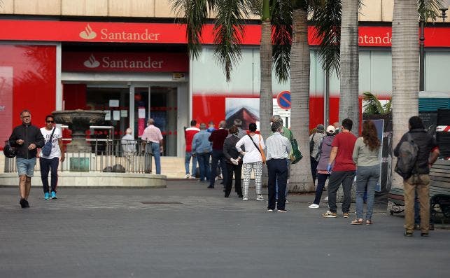 Numerosas personas hacen cola para entrar en una oficina bancaria del Banco Santander durante el estado de alarma. EFE/ Cristóbal García