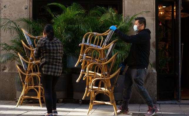Dos personas recogen sillas de una terraza, poco antes de conocerse la normativa de la Generalitat que obligaba al cierre de bares y restaurantes / EFE