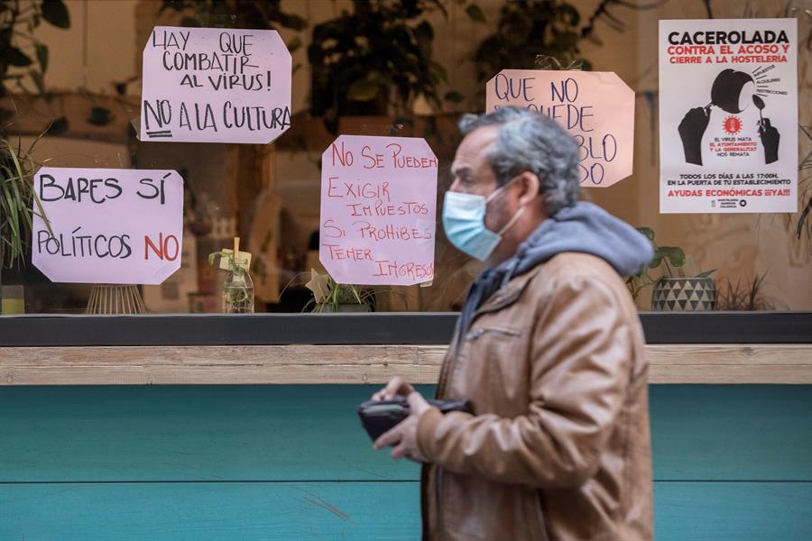 na persona pasa frente a un local de restauración con carteles de protesta por el cierre de la hostelería debido a las nuevas restricciones. EFE / Biel Aliño