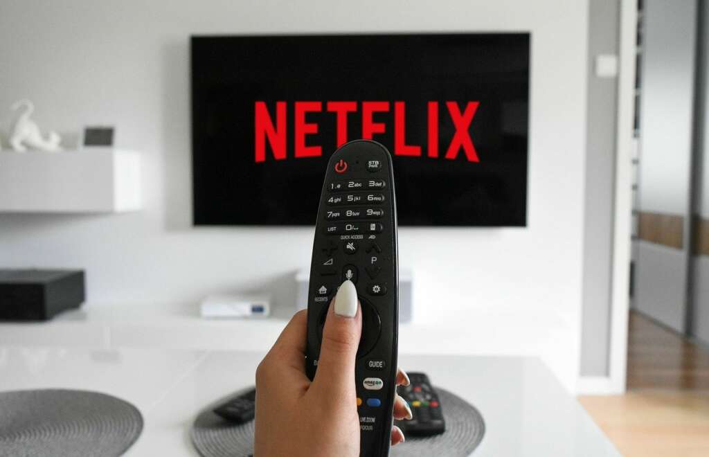 Imagen de un mando frente a un televisor que inicia Netflix