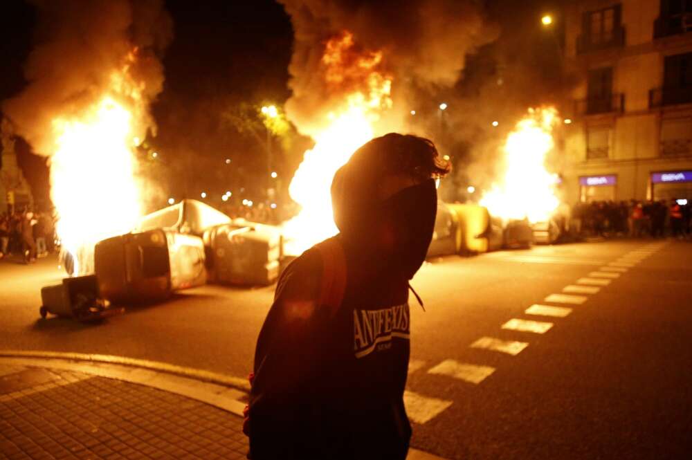 Un manifestante con contenedores ardiendo detrás en la cuarta noche de protestas por la detención del rapero Pablo Hasél, el 19 de febrero de 2021 en Barcelona | EFE/QG/Archivo