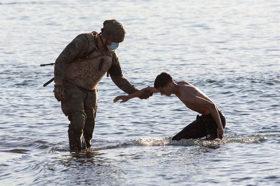  Un soldado del ejército ayuda a un inmigrante a su llegada a la playa de El Tarajal en Ceuta este miércoles. La frontera de Ceuta entre Marruecos y España ha amanecido con solo unas decenas de inmigrantes que intentan llegar a nado, una situación que difiere de la registrada hace dos días, cuando llegaron 8.000 personas, la mitad de las cuales han sido devueltas, según el Gobierno español. EFE/Brais Lorenzo