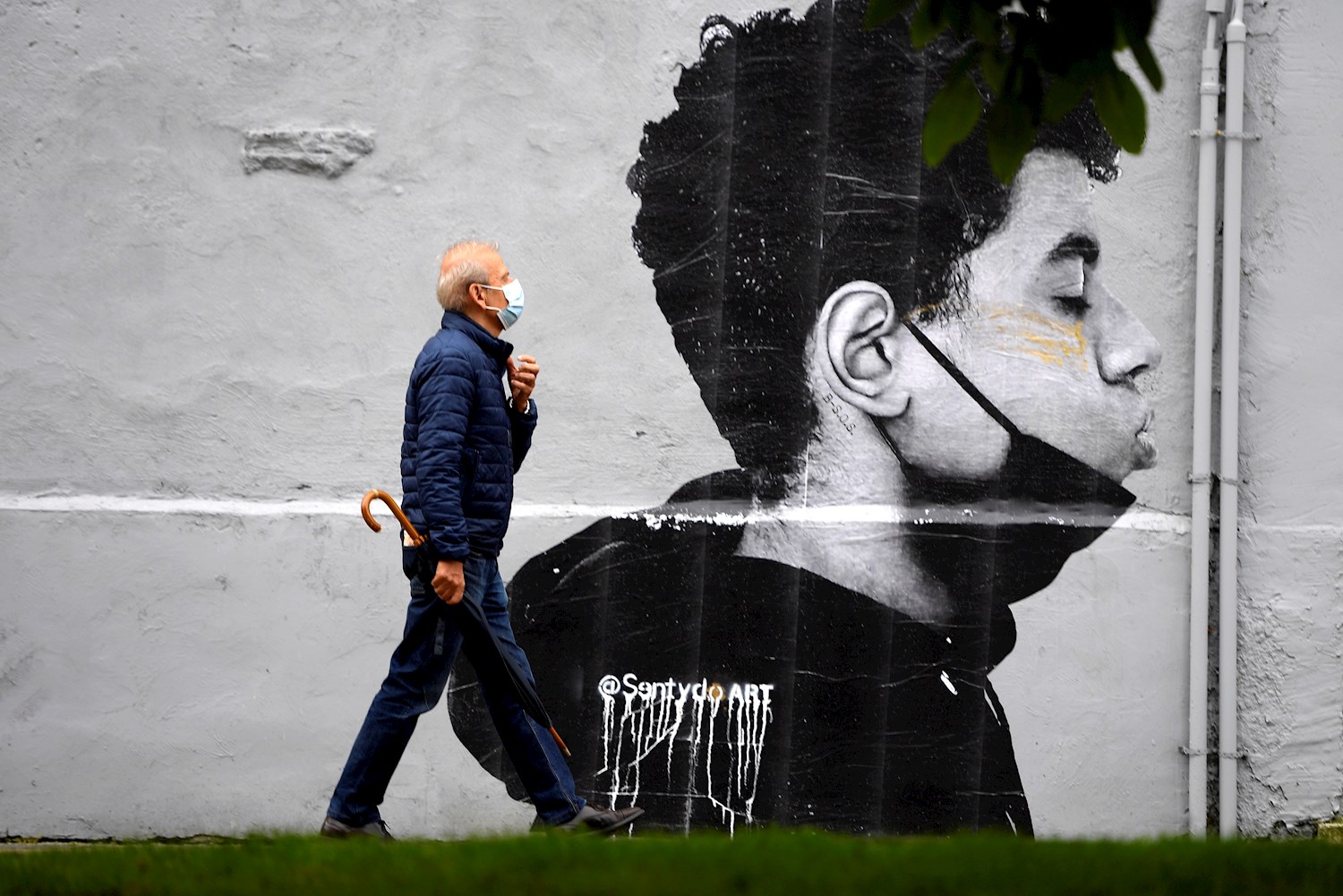 Un hombre con mascarilla camina delante de una obra del artista @Sentydo ART en una campaña dedicada a los besos sin mascarillas. EFE/ Eloy Alonso