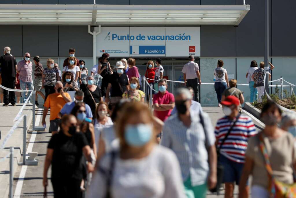 Centenares de ciudadanos llevan más de una hora esperando su turno para vacunarse en el hospital Enfermera Isabel Zendal, algunas refugiadas del sol y de las altas temperaturas bajo sus paraguas, mientras una caravana de coches en los alrededores del centro trata de aparcar. EFE/ Mariscal