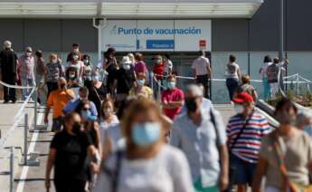 Centenares de ciudadanos llevan más de una hora esperando su turno para vacunarse en el hospital Enfermera Isabel Zendal, algunas refugiadas del sol y de las altas temperaturas bajo sus paraguas, mientras una caravana de coches en los alrededores del centro trata de aparcar. EFE/ Mariscal