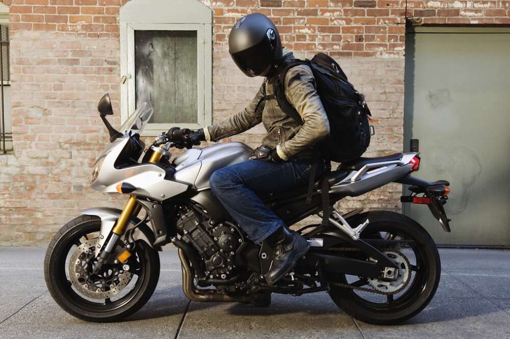 Un motorista sobre su moto con un casco negro y mochila