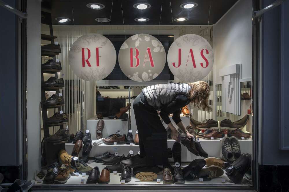 La empleada de una zapatería coloca el escaparate de rebajas de enero en una tienda de Pamplona. EFE/ Villar López