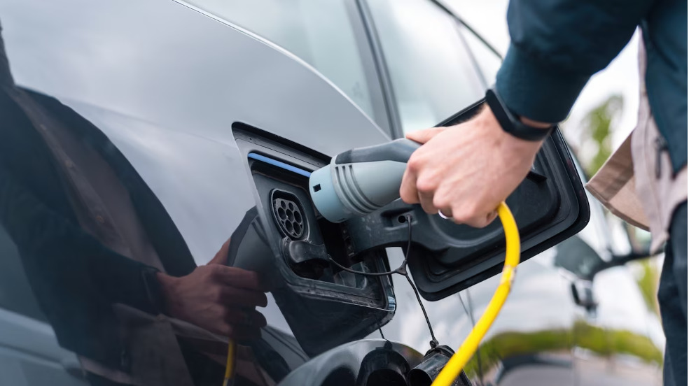 Hombre enchufando el cargador en un coche eléctrico en la estación de carga. Foto: Freepik