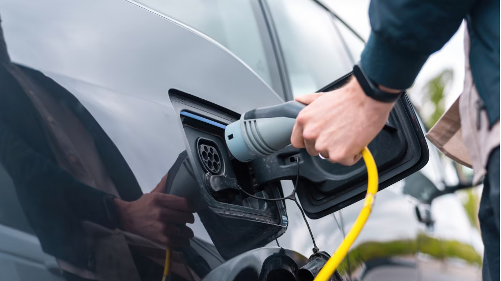 Hombre enchufando el cargador en un coche eléctrico en la estación de carga. Foto: Freepik