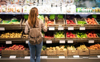 Una chica mira los estantes de fruta de un supermercado
