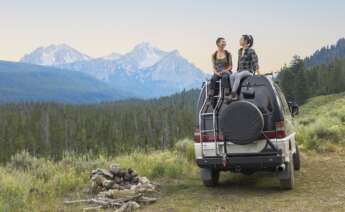 Dos chicas encima de un coche disfrutan de un paisaje de montaña