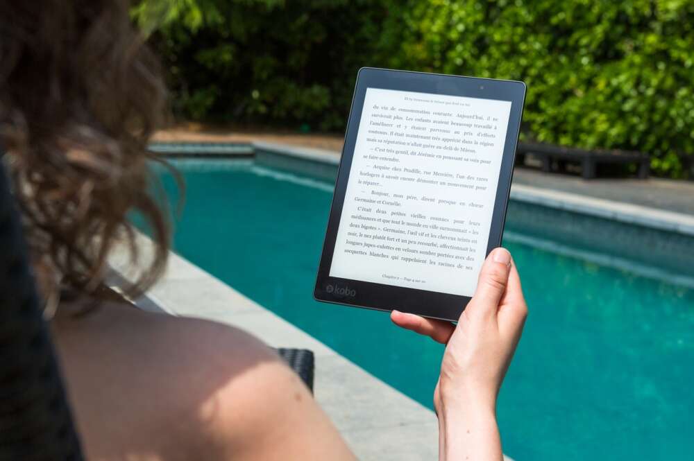 Una chica lee un libro electrónico en la piscina