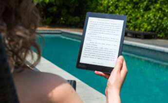 Una chica lee un libro electrónico en la piscina