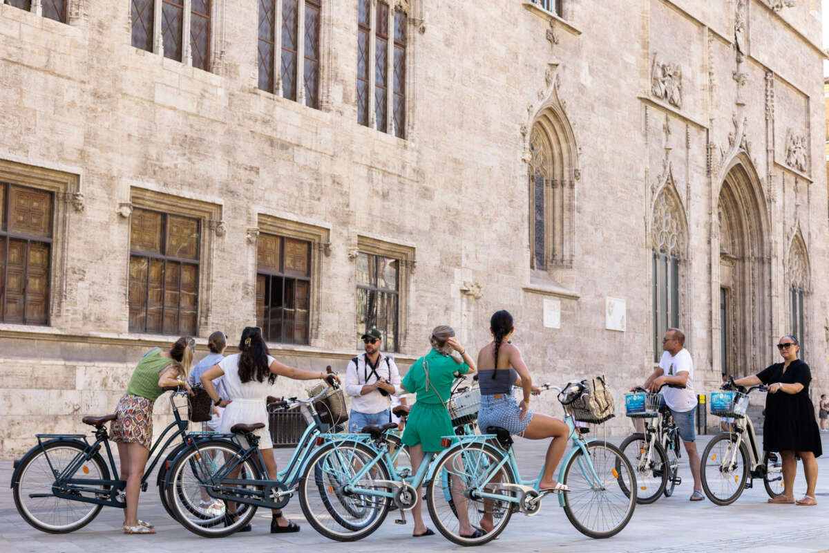 GRAFCVA5004. VALENCIA, 01/08/2023.- Un grupo de turistas en bicicleta escucha las explicaciones de su guía ante el edificio de La Lonja en el centro histórico de València, este martes uno de agosto. EFE/Biel Aliño
