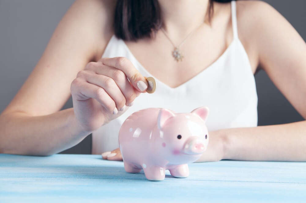 Una mujer guarda dinero en una hucha. Foto: Freepik.