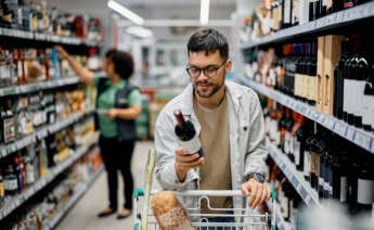 Un chico comprando una botella de alcohol en un supermercado
