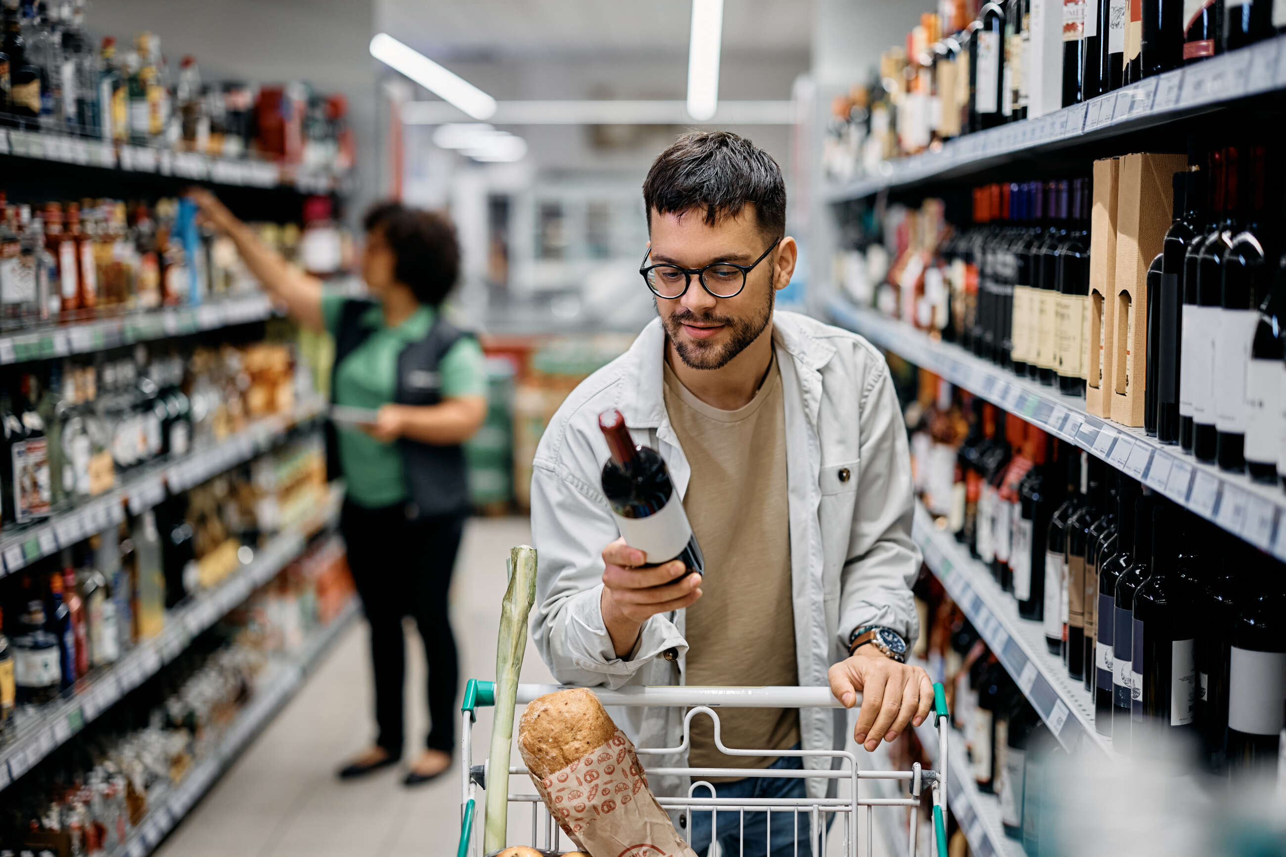 Un chico comprando una botella de alcohol en un supermercado