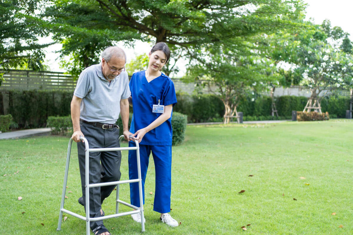 Una auxiliar de enfermería ayuda a un señor a caminar