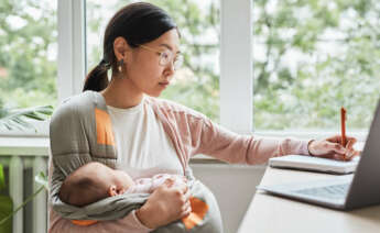 Una mujer trabajadora autónoma cuidando a su bebé mientras trabaja desde casa.