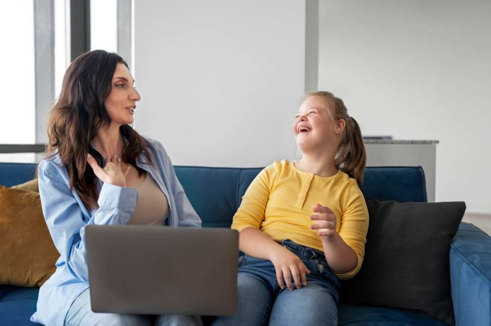 Una persona con un ordenador sonríe ante una persona con discapacidad. Foto: Freepik.