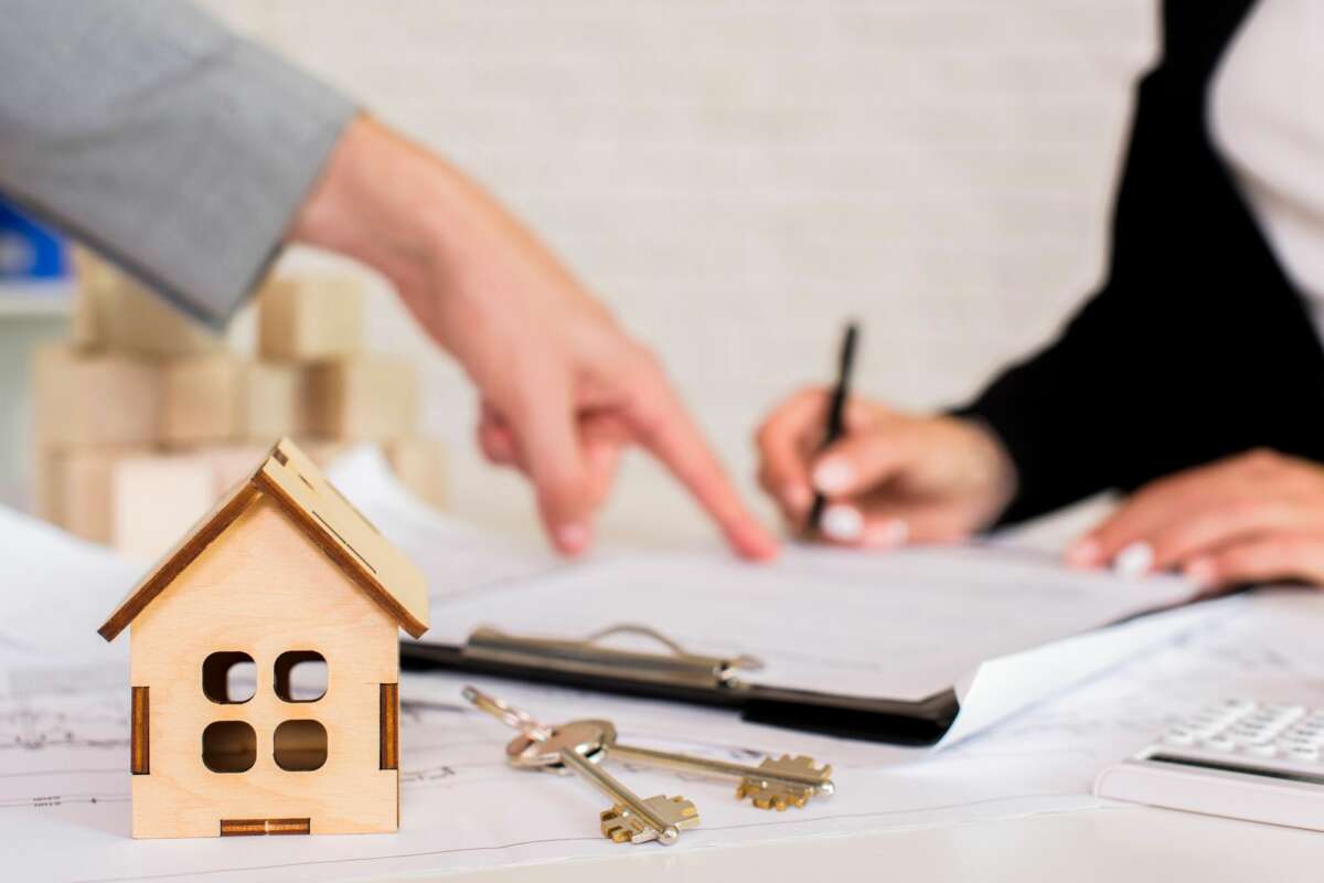Una persona señala un documento, mientras en la mesa hay una estructura de una casa y unas llaves. Foto: Freepik.